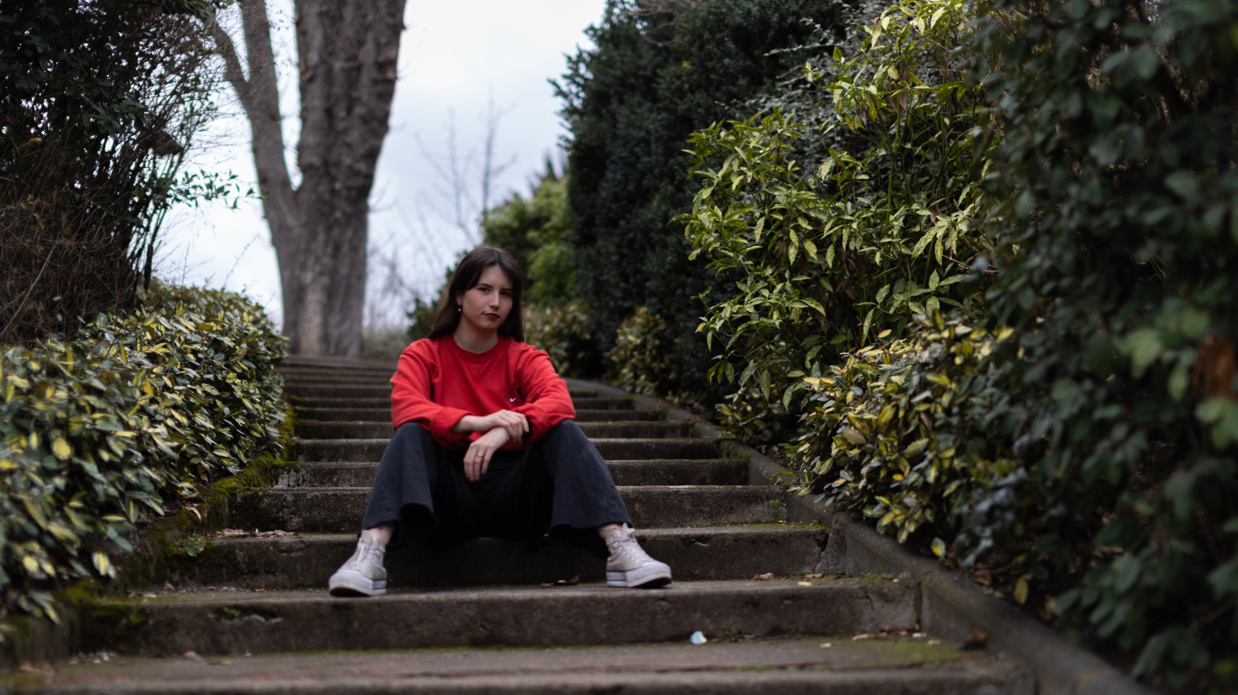 Une jeune femme assise sur des marches de pierre dans un sous-bois, les bras posés sur les genoux.
