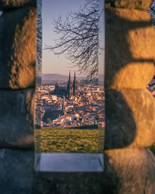 Vue d'une ville au crépuscule cadrée dans l'ouverture d'une sculpture de pierre, cathédrale au centre.